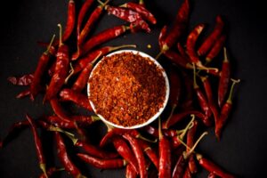 Red chili powder and whole chilies on dark background, showcasing spice and flavor.